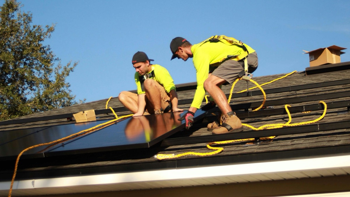 Two installers positioning a solar panel on a residential shingle roof