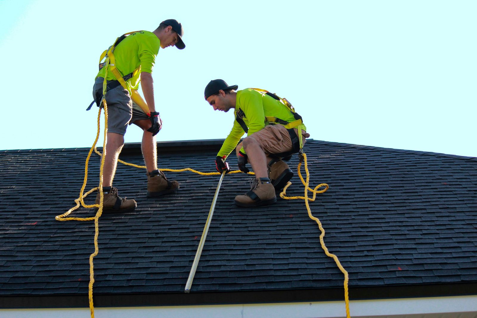 Two installers measuring a shingle roof before a solar installation