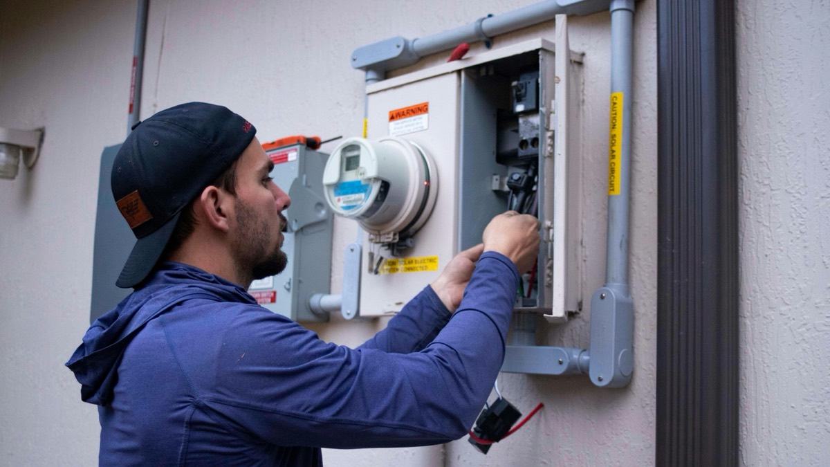 Technician connecting an outdoor electrical meter and disconnect box for a solar system